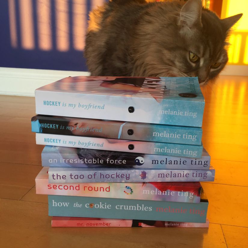 A most adorable floofy baby kitty thoroughly investigating a vertical stack of Melanie's books.