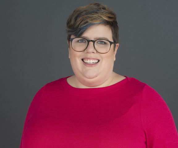 The fabulous Alli Temple has submitted a stunning headshot. She is a white woman with light brown hair with a bit of fashion highlight flare in a shorter swirl-type of haircut and the most amazing fuchsia crew-neck top. Also she is wearing really excellent glasses. I am not a fashion person so I don't know how to describe them to their full potential, but they are excellent.